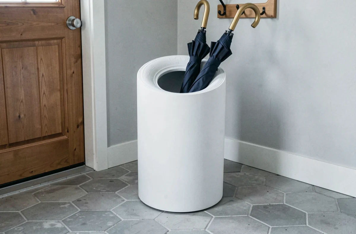 Porte-parapluies d'entrée fabriqué à partir d'un pneu peint en blanc mat avec insert doré sur carrelage hex